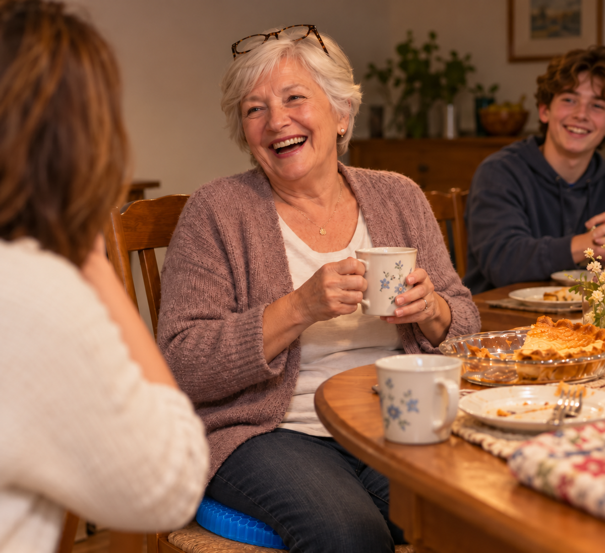 Grandmother laughing with family at the dinner table, sitting on a blue honeycomb gel cushion
