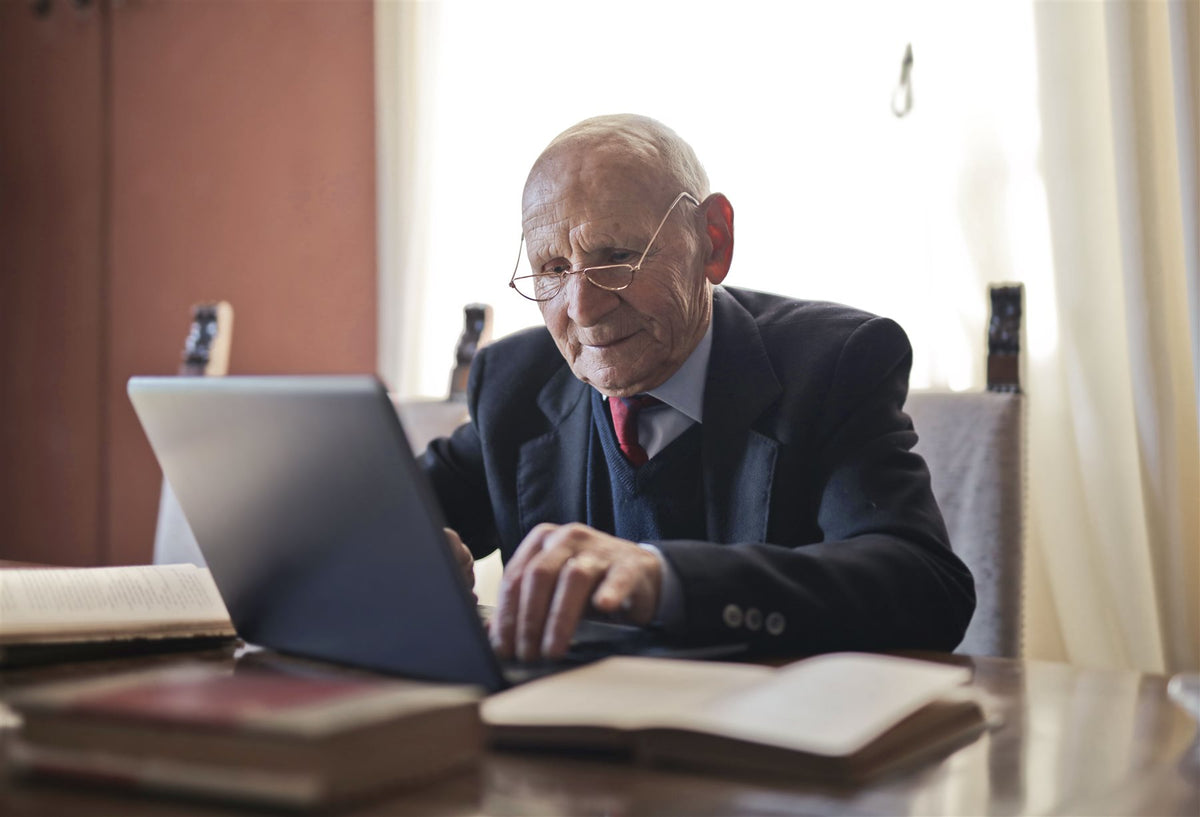 Older man in a suit working on a laptop at a wooden desk