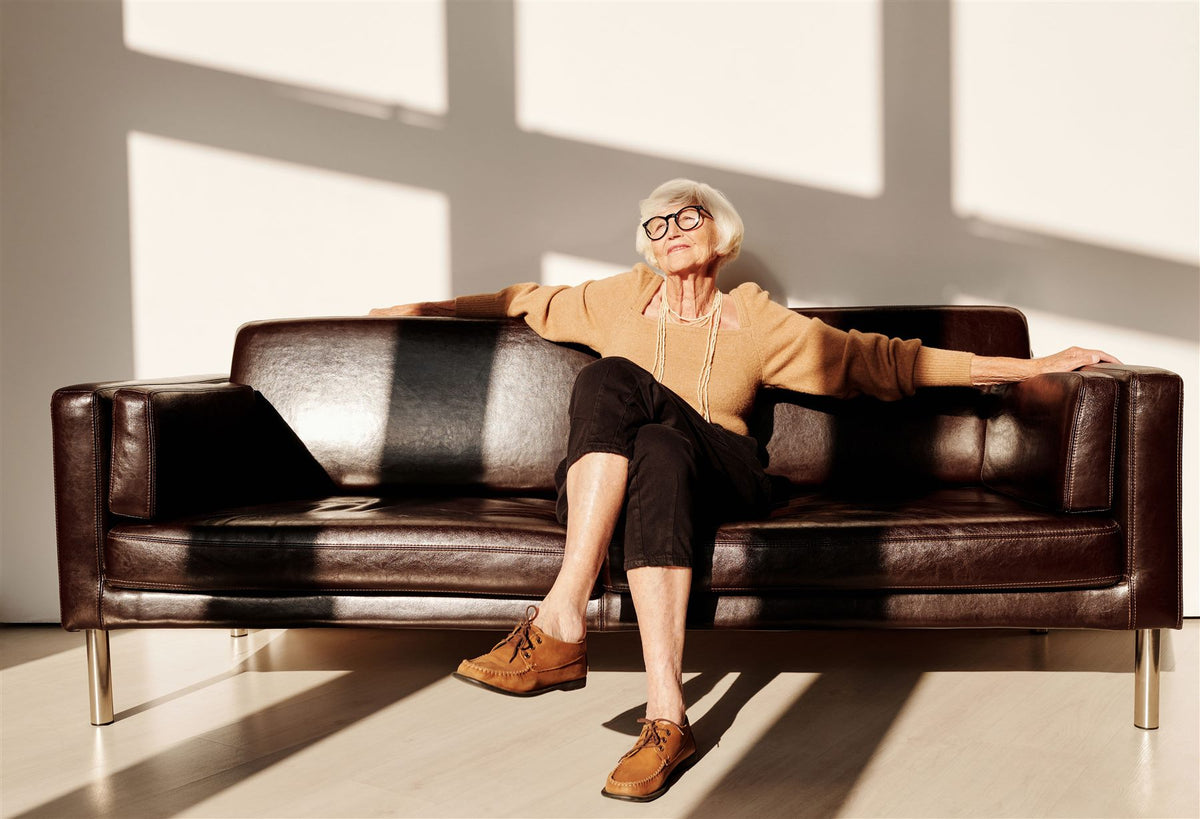 Smiling older woman relaxing on a leather sofa in a sunny living room